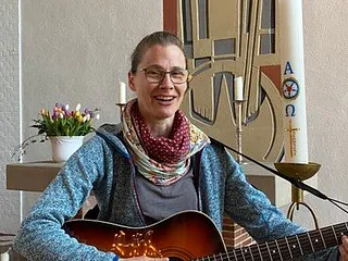 Peggy Luck lächelt und spielt Gitarre in einer Kirche.