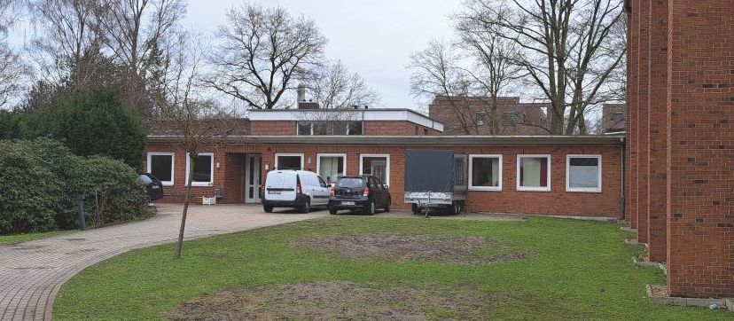 Einstöckiges Backsteingebäude mit geparkten Autos und einem Anhänger.