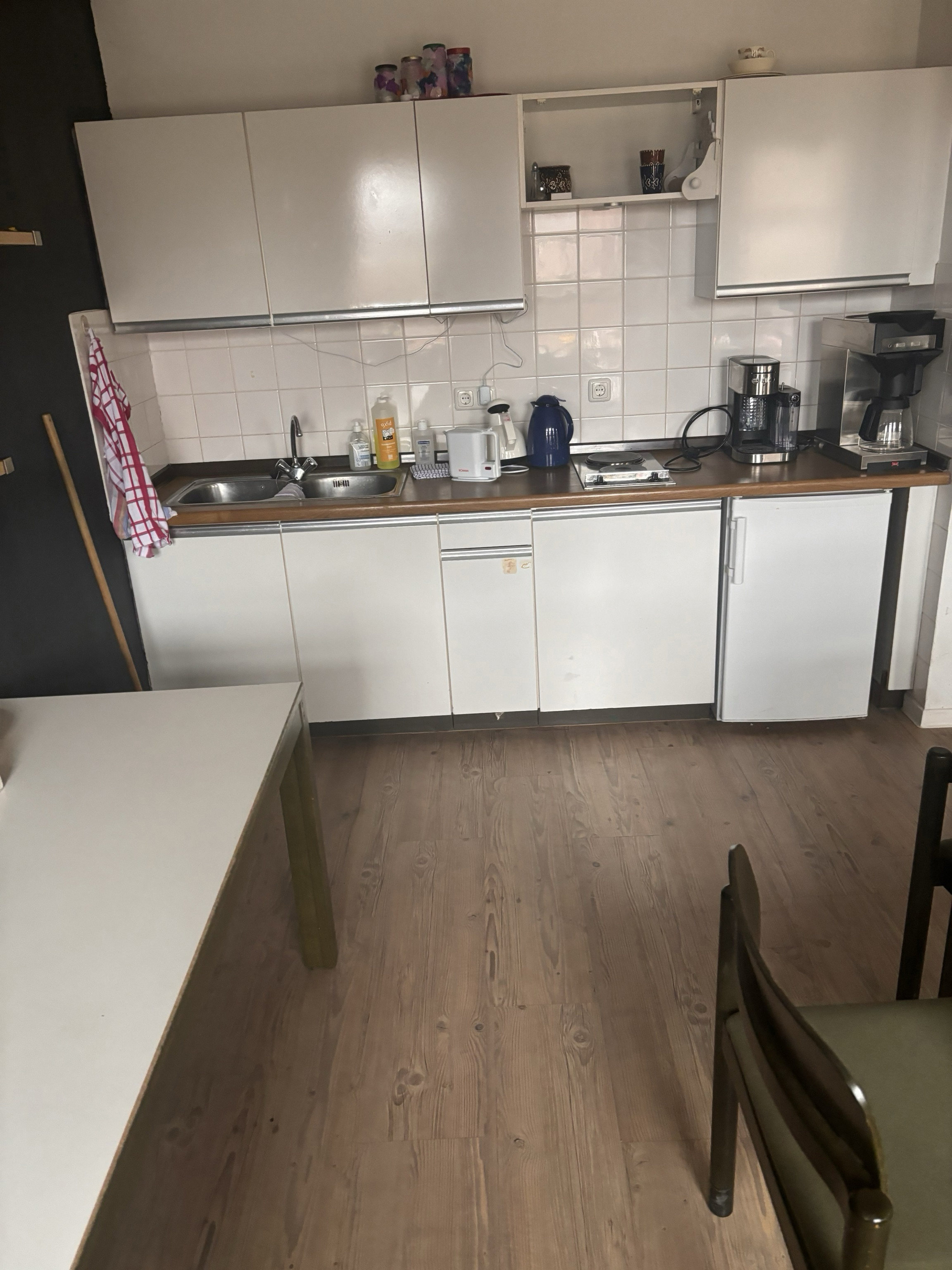 Kleine Küche mit weißen Schränken und Geräten, Holzboden.