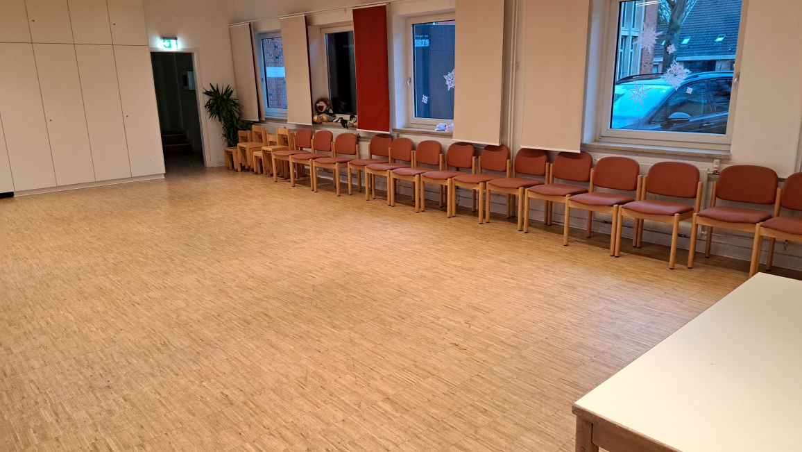 Leerer Saal mit Stuhlreihen und Holzboden.