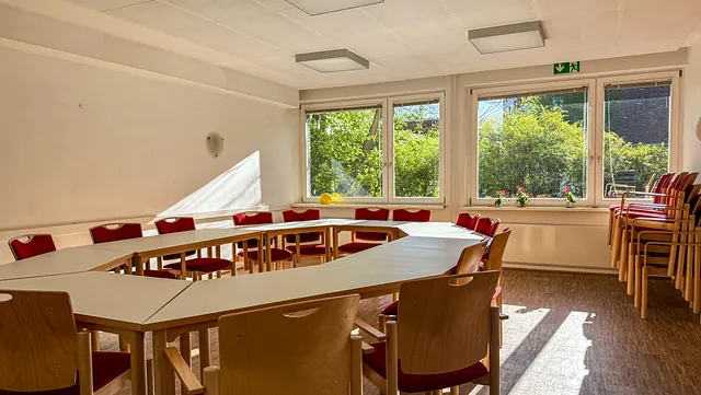 Konferenzraum mit einem offenen, U-förmigen Tisch und blauen Stühlen.