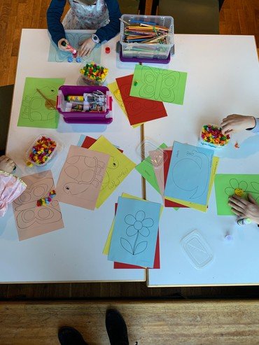 Kinder basteln bunte Blumen Collagen an einem weißen Tisch.