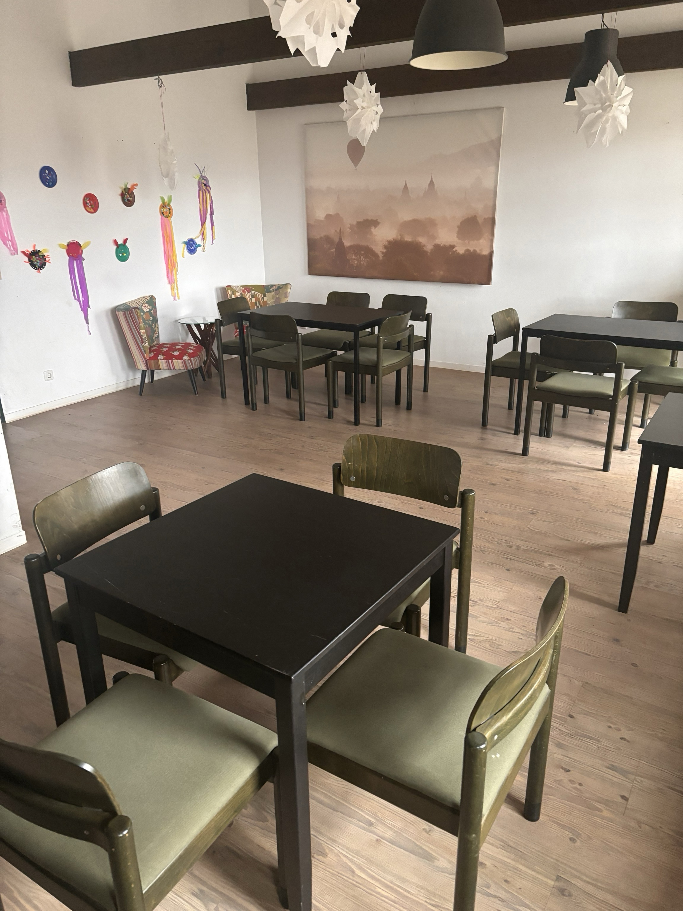 Möblierter Essbereich mit dunklen Tischen und grünen Stühlen.