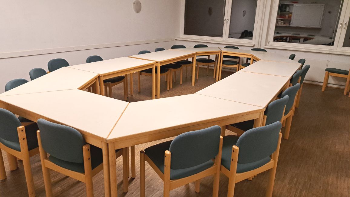 Konferenzraum mit einem offenen, U-förmigen Tisch und blauen Stühlen.