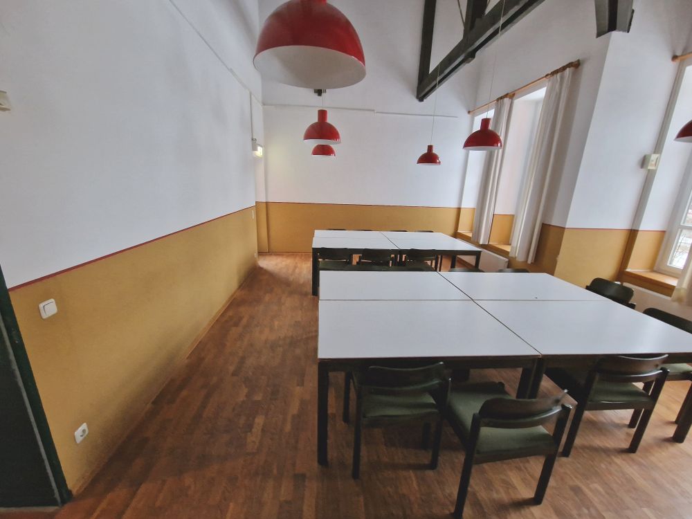 Leerer Speisesaal mit Tischen und Stühlen, rote Hängelampen.