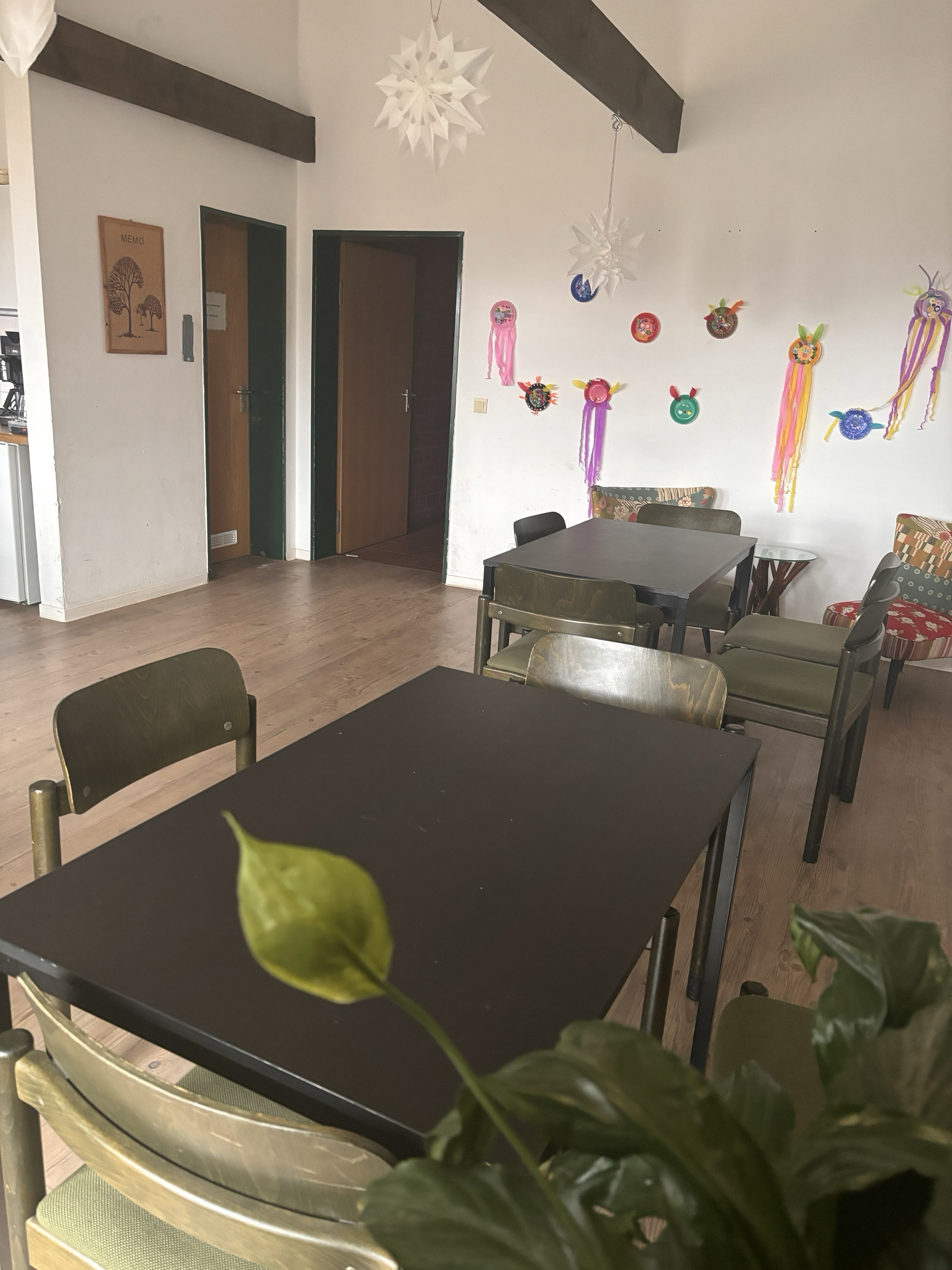 Schlichter Essbereich mit dunklen Tischen, grünen Stühlen und Kinderzeichnungen.