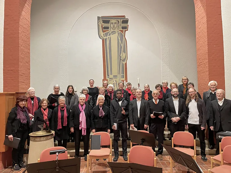 Erwachsenenchor posiert in einer Kirche mit Christusfigur im Hintergrund.