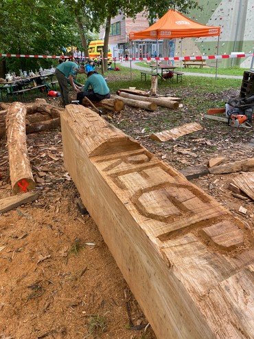 Holzschnitzer bearbeiten große Eichenbalken im Freien mit Werkzeugen.