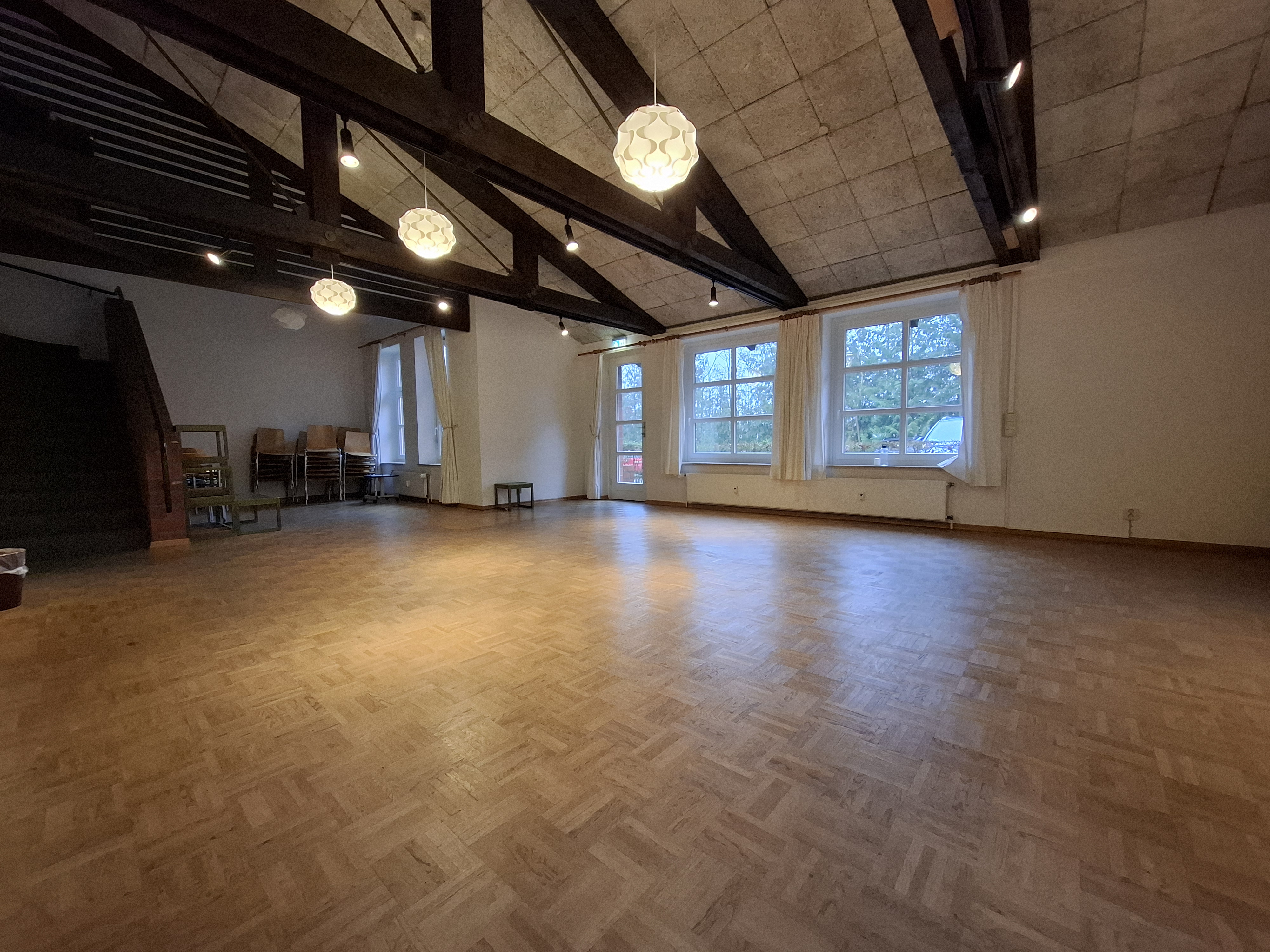 Großer, leerer Saal mit Parkettboden und freiliegenden Holzbalken.