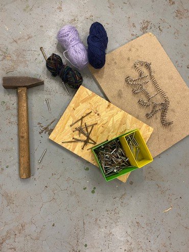 Hammer, Nägel, Garn und Dinosaurier-Fadenkunstprojekt auf Brettern.