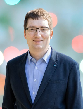 Porträt von Pierre Poignant, lächelnder Mann mit Brille und blauem Hemd.